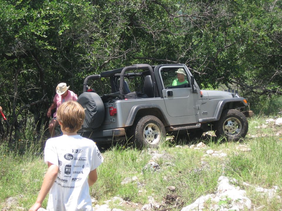 Silver Jeep Wrangler with a spare tire on the back, parked on a rocky, grassy trail