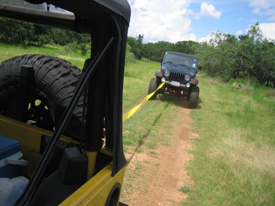 Blue Jeep Wrangler being towed by yellow Jeep Wrangler on a dirt path