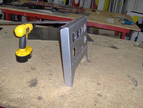 1978 Ford Bronco - A metal bracket with holes and a cordless drill are on a workbench.