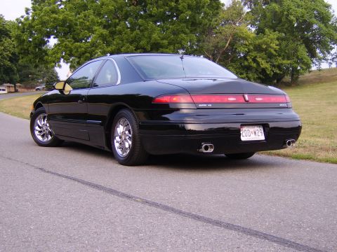1996 Mercury Grand Marquis - A black Lincoln Mark VIII is shown from the rear quarter angle, parked on a paved road with trees in the background.