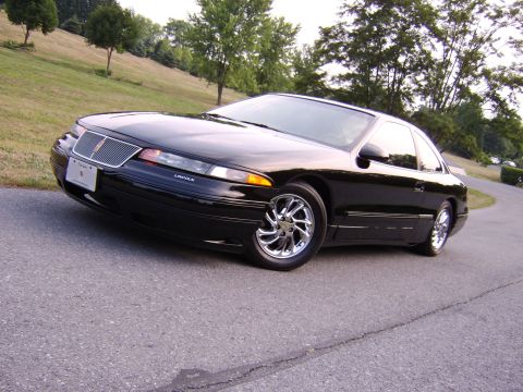 1996 Mercury Grand Marquis - This black Lincoln coupe has chrome wheels and is parked on a road with a grassy hill behind it.