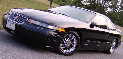1996 Mercury Grand Marquis - A black Lincoln Mark VIII coupe is parked on a paved surface with a grassy hill and trees in the background.
