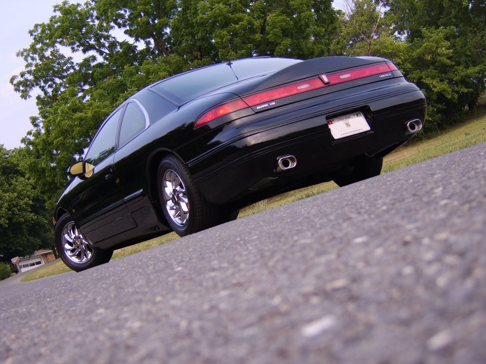 Black Lincoln Mark VIII coupe rear-quarter view on pavement with chrome wheels