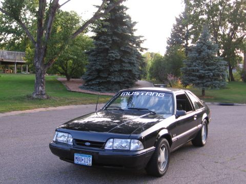 1989 Ford Mustang - A black 1989 Ford Mustang hatchback is parked on a suburban street.
