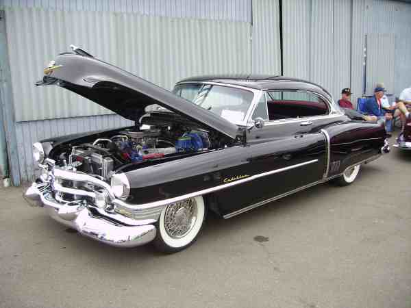 Black coupe with hood open, showing engine and chrome grille. Whitewall tires