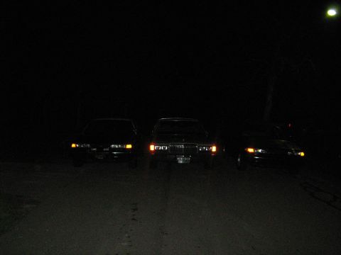 1988 Mercury Grand Marquis - Three cars are parked at night, with the middle vehicle appearing to be a 1988 Mercury Grand Marquis.