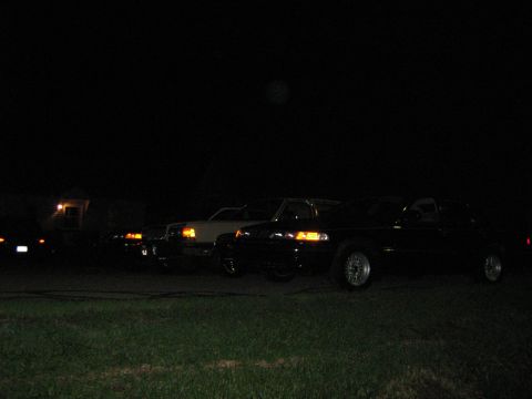 1988 Mercury Grand Marquis - Several cars are parked outside at night, with headlights on.