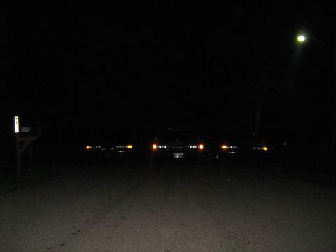 1988 Mercury Grand Marquis - Several vehicles are parked on a street at night, illuminated by their headlights and a nearby streetlamp.