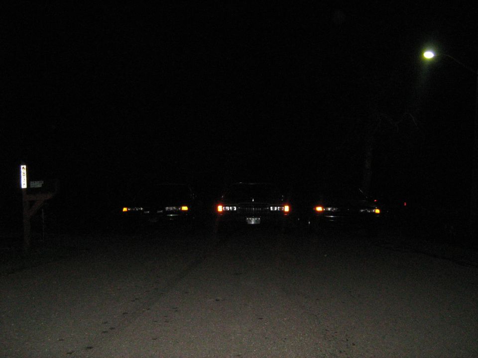 three cars parked on a dark road at night, headlights on