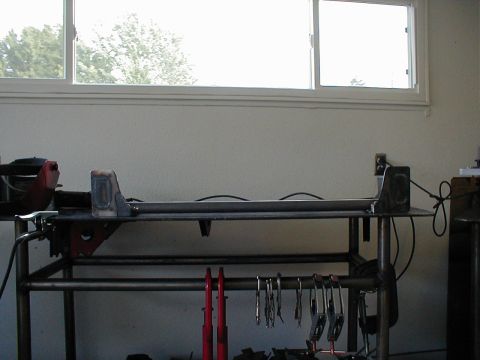 1996 Ford Bronco - A metal frame, likely a vehicle part, rests on a workbench under a window.