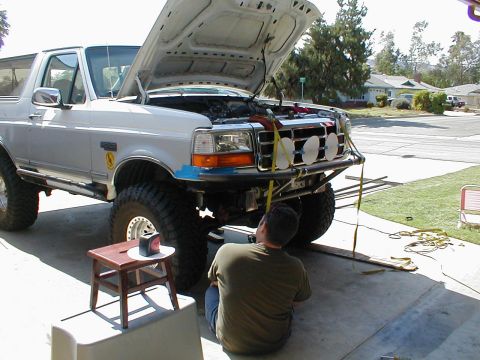 1996 Ford Bronco - A person works on the engine of a 1996 Ford Bronco, which is lifted with its hood open.