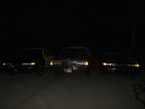 1988 Mercury Grand Marquis - Three sedans are parked in a line at night, with the middle vehicle identified as a 1988 Mercury Grand Marquis.