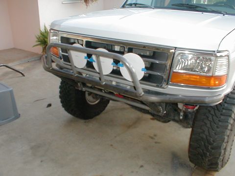 1996 Ford Bronco - The front end of a white truck is shown with a custom bumper and auxiliary lights. The grille and headlights are visible.