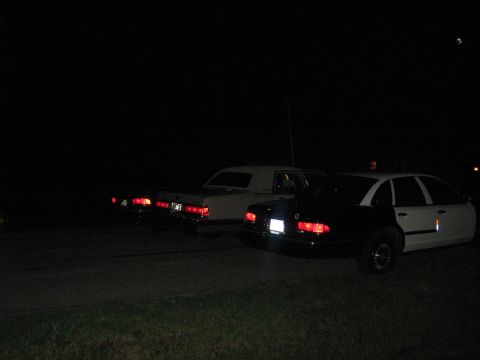 1988 Mercury Grand Marquis - Three vehicles are parked at night, with the closest being a black and white police car.