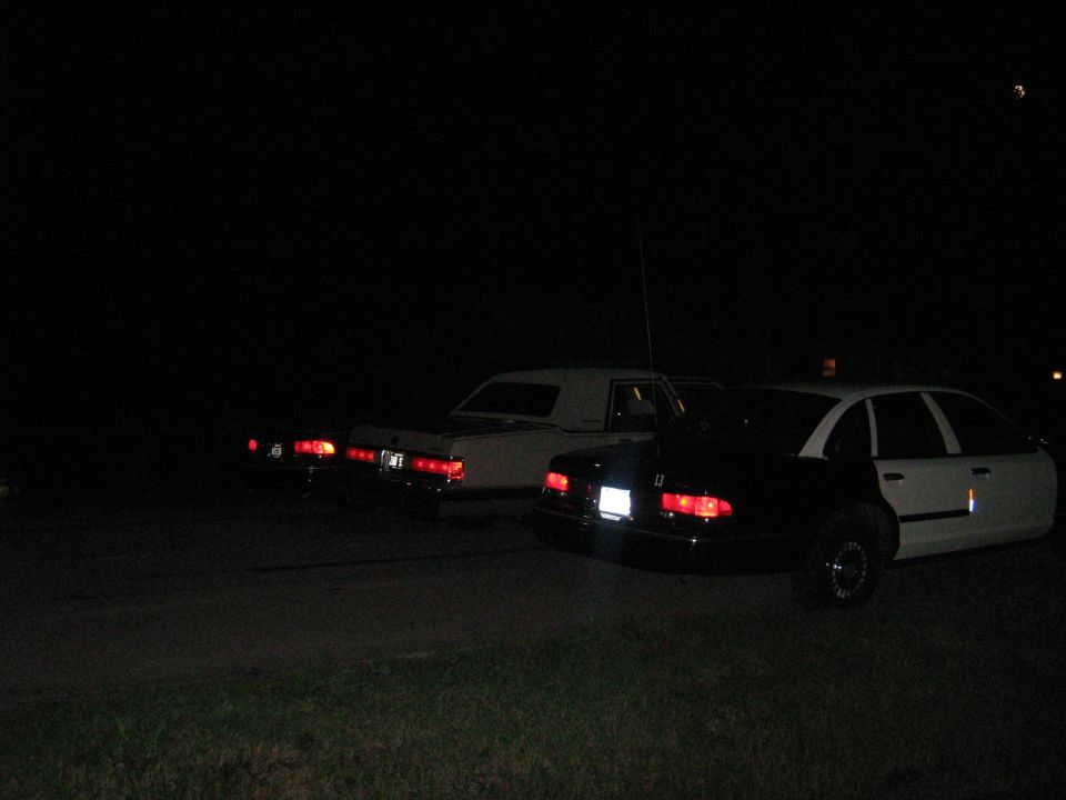 Rear view of a black and white police car and two sedans at night