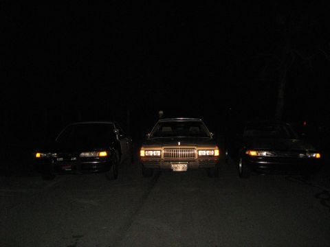 1988 Mercury Grand Marquis - Three sedans parked in a row at night, with headlights on.