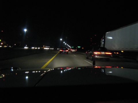 1988 Mercury Grand Marquis - Nighttime driver's-eye view over a car's hood on a multi-lane highway, with taillights reflecting off the paint, a semi trailer passing in…
