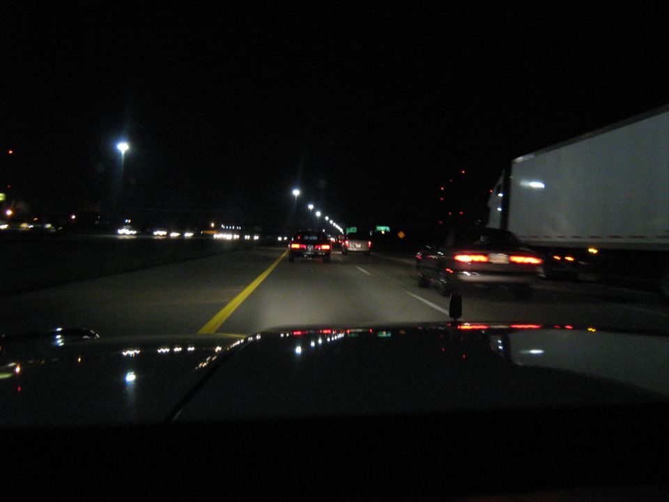 Night highway view over a car hood with taillights and a semi trailer alongside