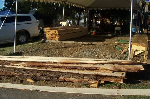 1994 Ford F-150 - A white pickup truck with a camper shell is parked next to stacks of lumber under a tent.