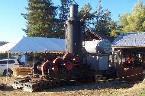 1994 Ford F-150 - A large steam engine with a winch mechanism and a water tank labeled "Rhodes Small Mining Reel" is displayed outdoors.