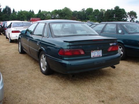 1993 Ford Taurus - Rear view of a dark green sedan parked on dry grass, with other vehicles visible.