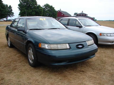 1993 Ford Taurus - A green Ford Taurus is parked on dry grass with another car behind it.