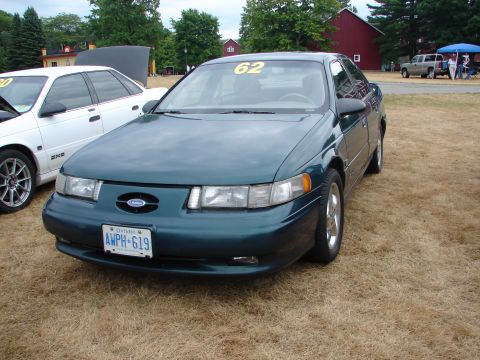1993 Ford Taurus - A green Ford Taurus sedan is parked on dry grass, with another car in the background.