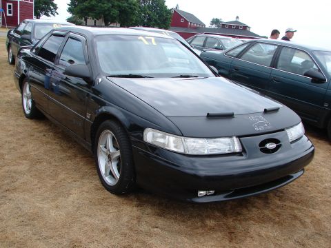 1993 Ford Taurus - A black sedan is parked on a grassy area, with a car cover obscuring the front of the hood.