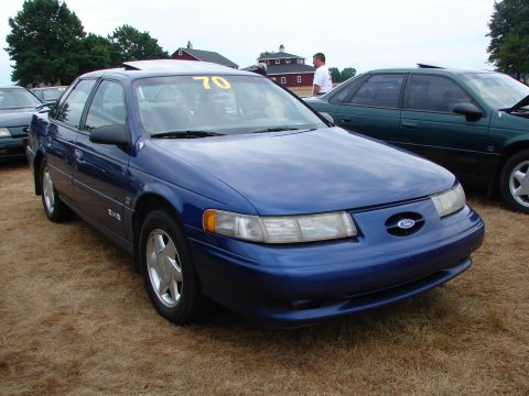 1993 Ford Taurus - A blue 1993 Ford Taurus is parked on dry grass, with a yellow number 70 visible on its windshield.