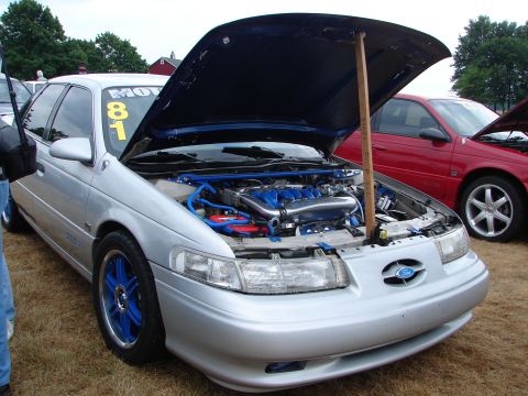1993 Ford Taurus - A silver 1993 Ford Taurus is displayed with its hood open, revealing a customized engine bay and bright blue components.