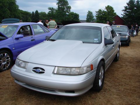 1993 Ford Taurus - A silver 1993 Ford Taurus sedan with a prominent hood scoop is parked at a car show.