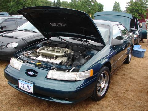 1993 Ford Taurus - A 1993 Ford Taurus SHO with its hood open, revealing the engine and a prominent SHO badge on the underside of the hood.