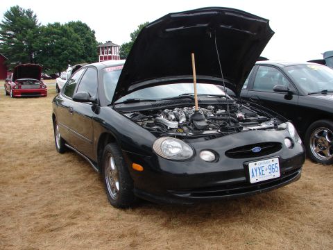 1993 Ford Taurus - A black sedan is parked on dry grass with its hood open, revealing the engine compartment.
