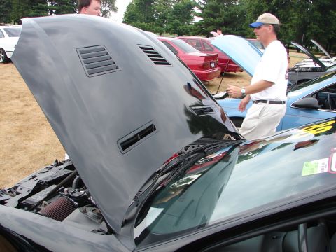 1993 Ford Taurus - A black car's hood is open, revealing the engine compartment, with other vehicles and attendees visible.