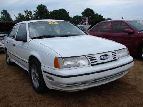 1993 Ford Taurus - Front view of a white 1993 Ford Taurus at a car show, with a red car in the background.
