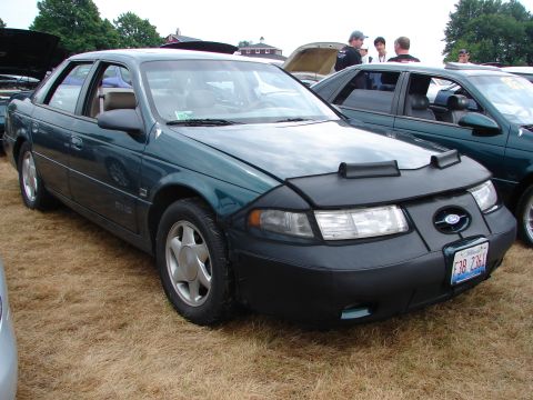1993 Ford Taurus - A green sedan with a car bra is parked on dry grass next to another car.