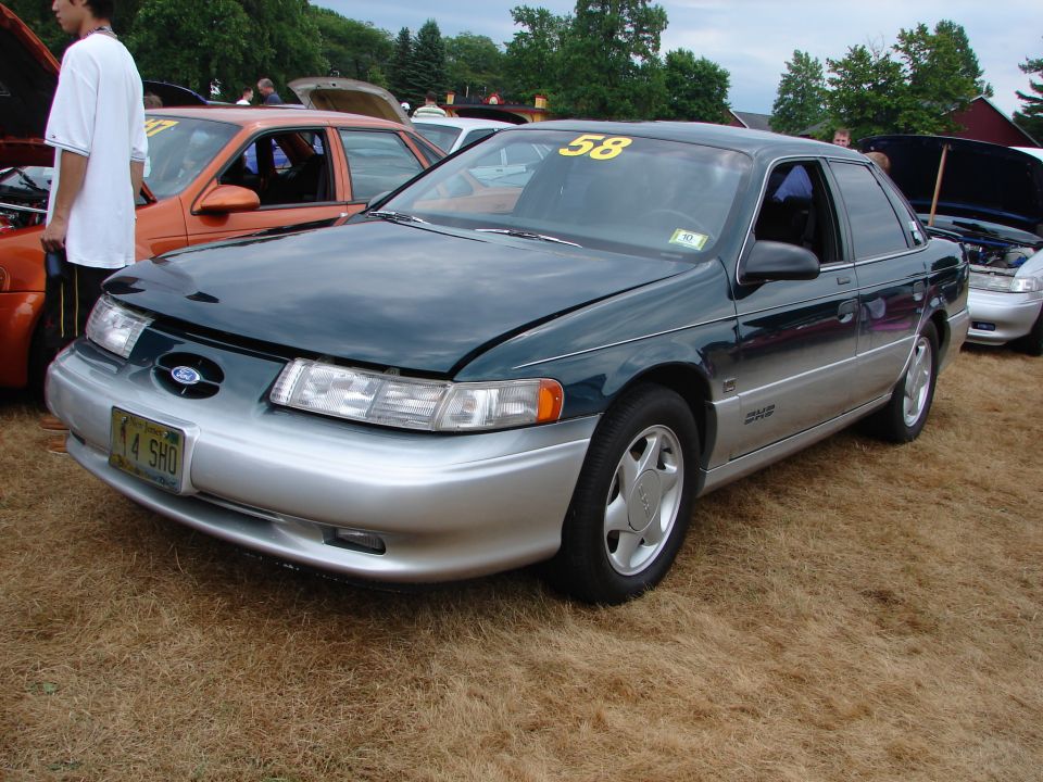 1993 Ford Taurus SHO with a yellow 58 sticker on the windshield, parked on dry grass