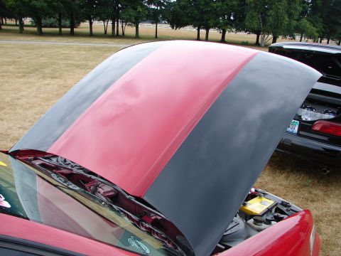 1993 Ford Taurus - A red car with its hood open, showing the engine compartment and a yellow battery, with another car visible behind it.