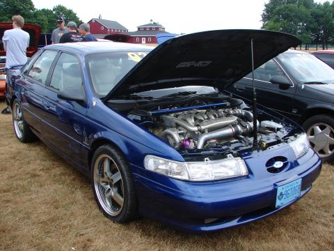 1993 Ford Taurus - A blue 1993 Ford Taurus SHO is displayed with its hood open, revealing a custom engine setup and turbo setup.