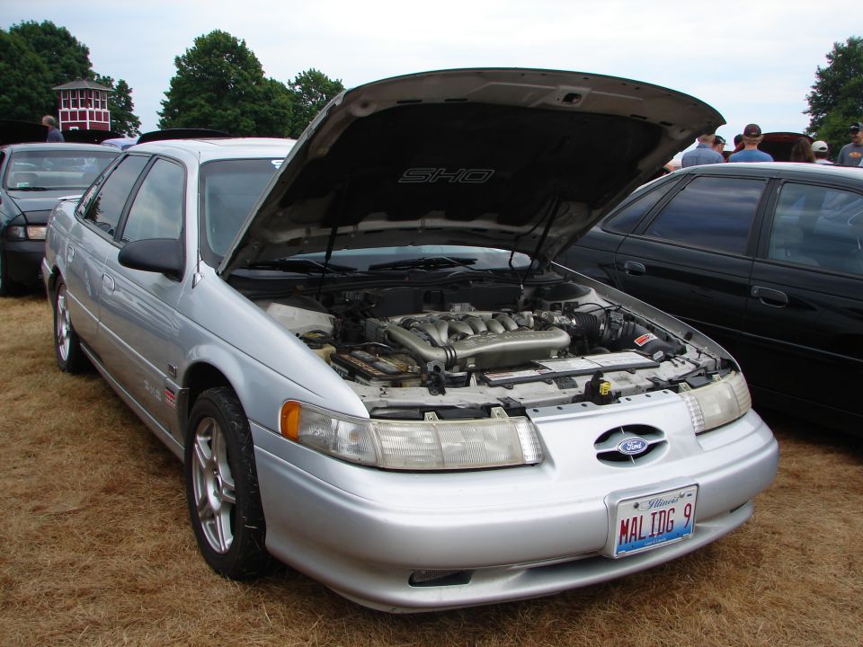 Silver 1993 Ford Taurus SHO with hood open, showing the engine. Another car is parked next to it