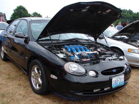 1993 Ford Taurus - A black Ford Taurus with its hood open reveals a modified engine, parked at an outdoor event.