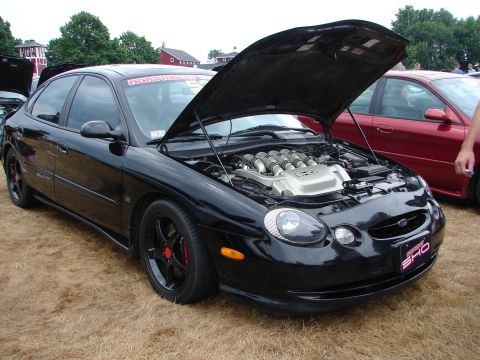1993 Ford Taurus - Black Ford Taurus SHO with hood open, revealing its V8 engine, parked next to a red car.