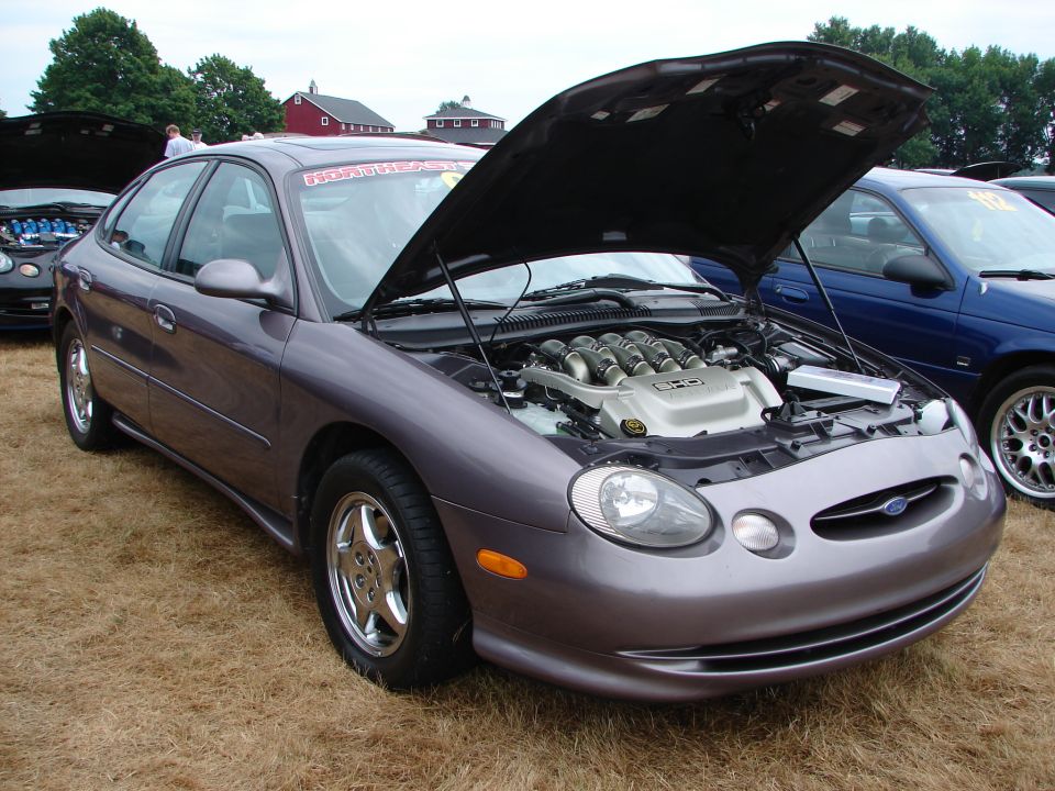 Purple Ford Taurus with hood open, revealing V8 engine. Another car is parked to the right