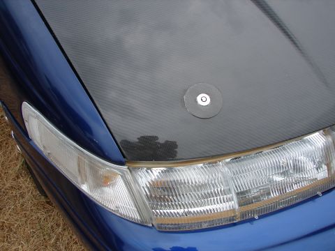 1993 Ford Taurus - Close-up of a blue car's front end, showing a carbon fiber hood and a clear headlight assembly.