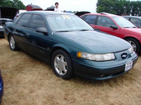 1993 Ford Taurus - A dark teal 1993 Ford Taurus sedan is parked on a grassy field, with other vehicles visible in the background.