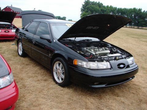 1993 Ford Taurus - A black 1993 Ford Taurus SHO is displayed with its hood open, revealing the engine, at an outdoor car show.