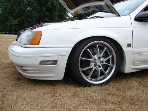 1993 Ford Taurus - Front quarter panel and custom wheels of a white 1993 Ford Taurus with the hood open.