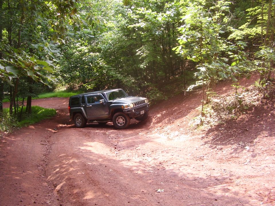Dark blue Hummer H3 on a dirt road in a wooded area