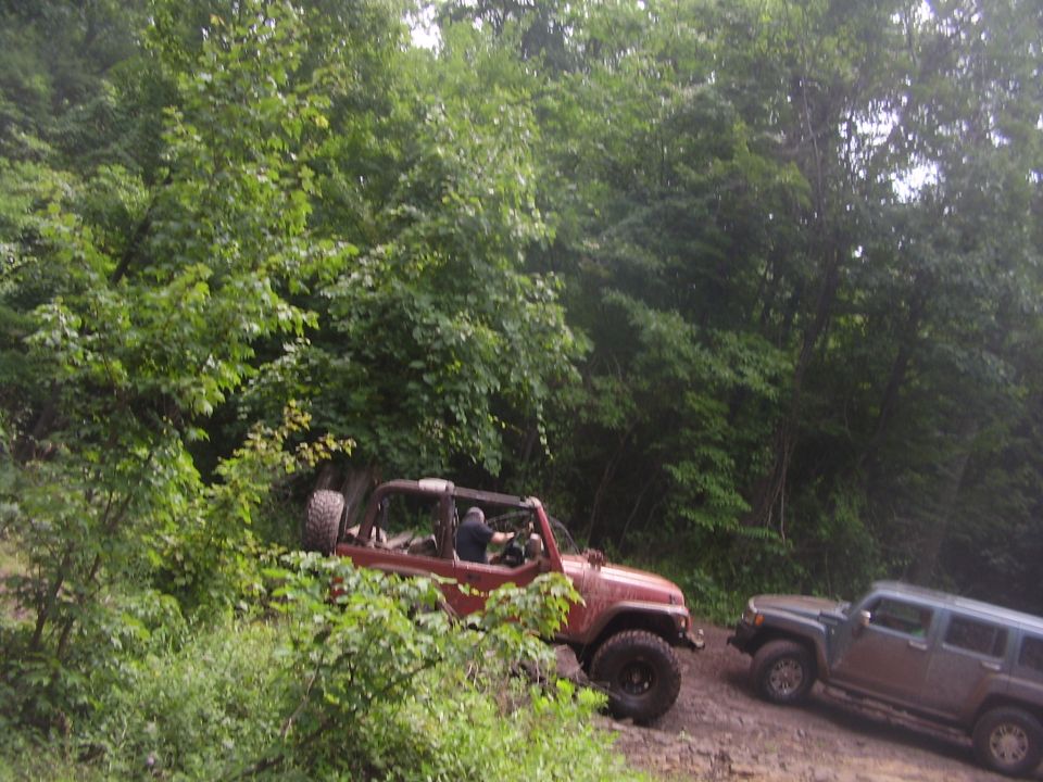 Red Jeep Wrangler and grey Hummer on a dirt road with trees