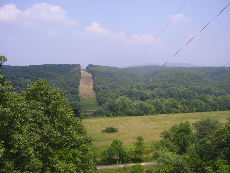 Overhead power lines cross a wide valley with a cleared hillside